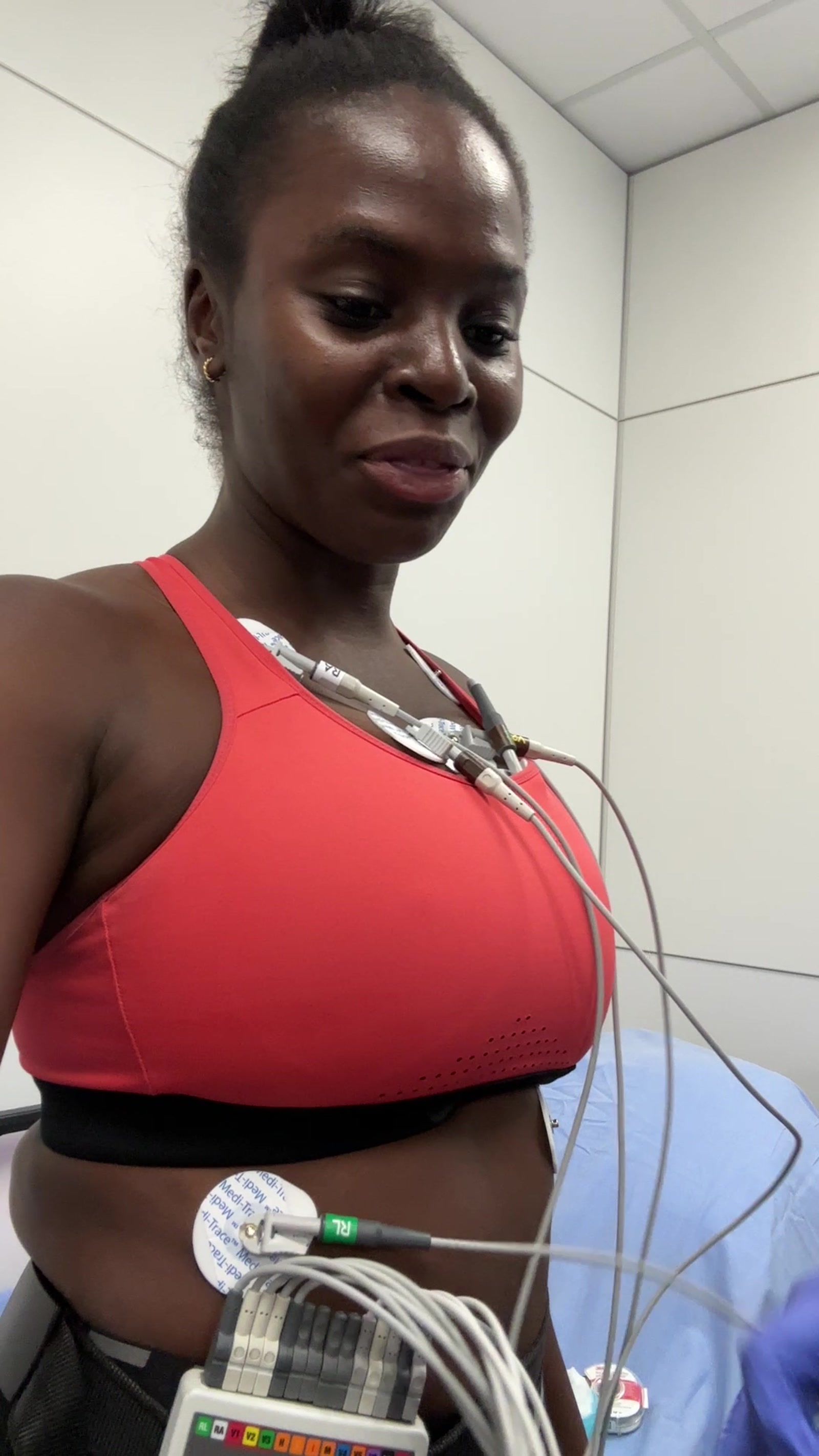 Neola standing fully wired with 12-lead ECG monitor — red sports bra, electrode wires across chest