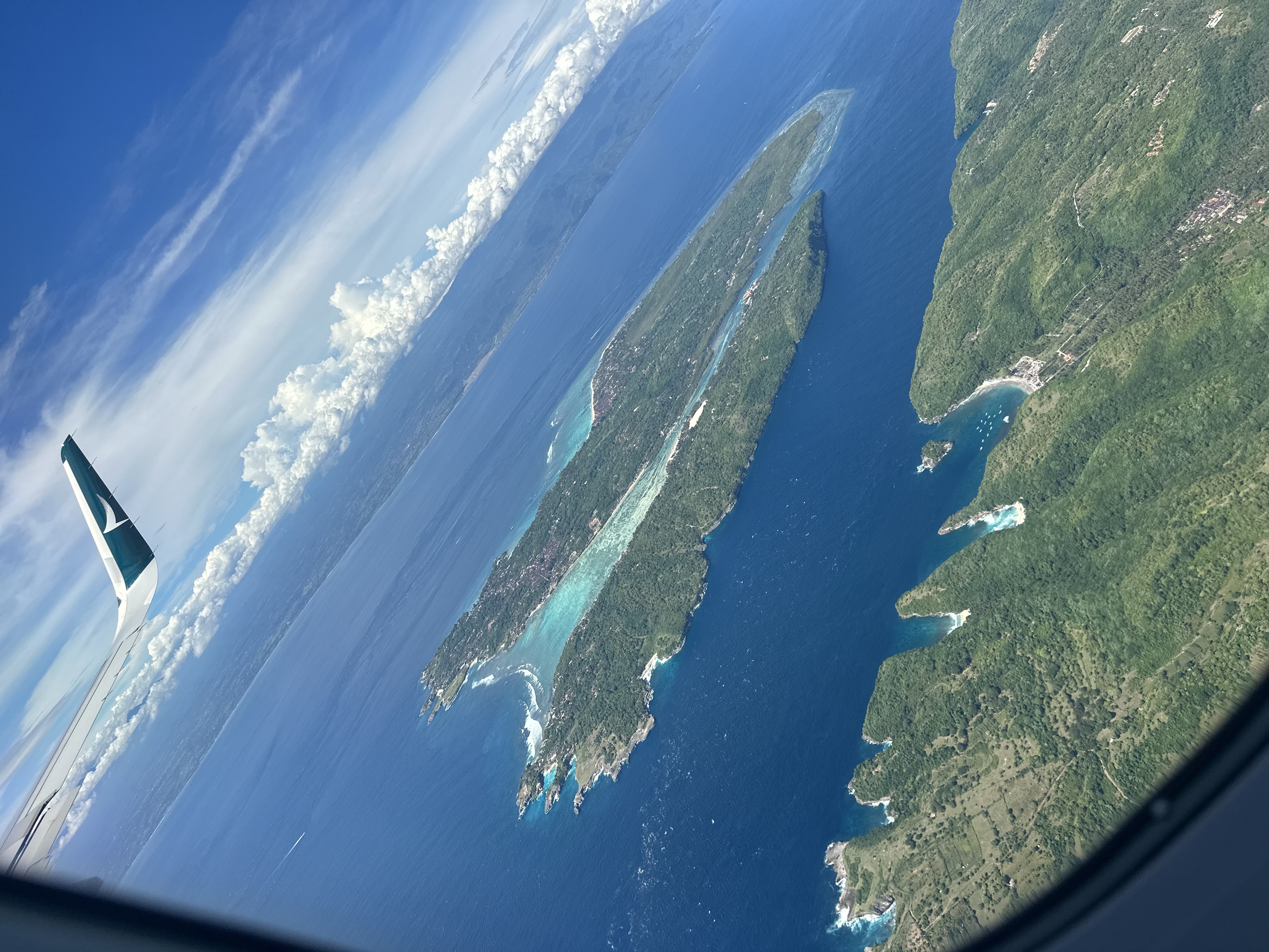 Neola Husbands en route to Bali, Indonesia — aerial view of Bali from a Cathay Pacific window seat, returning July 2026 for six weeks with her son