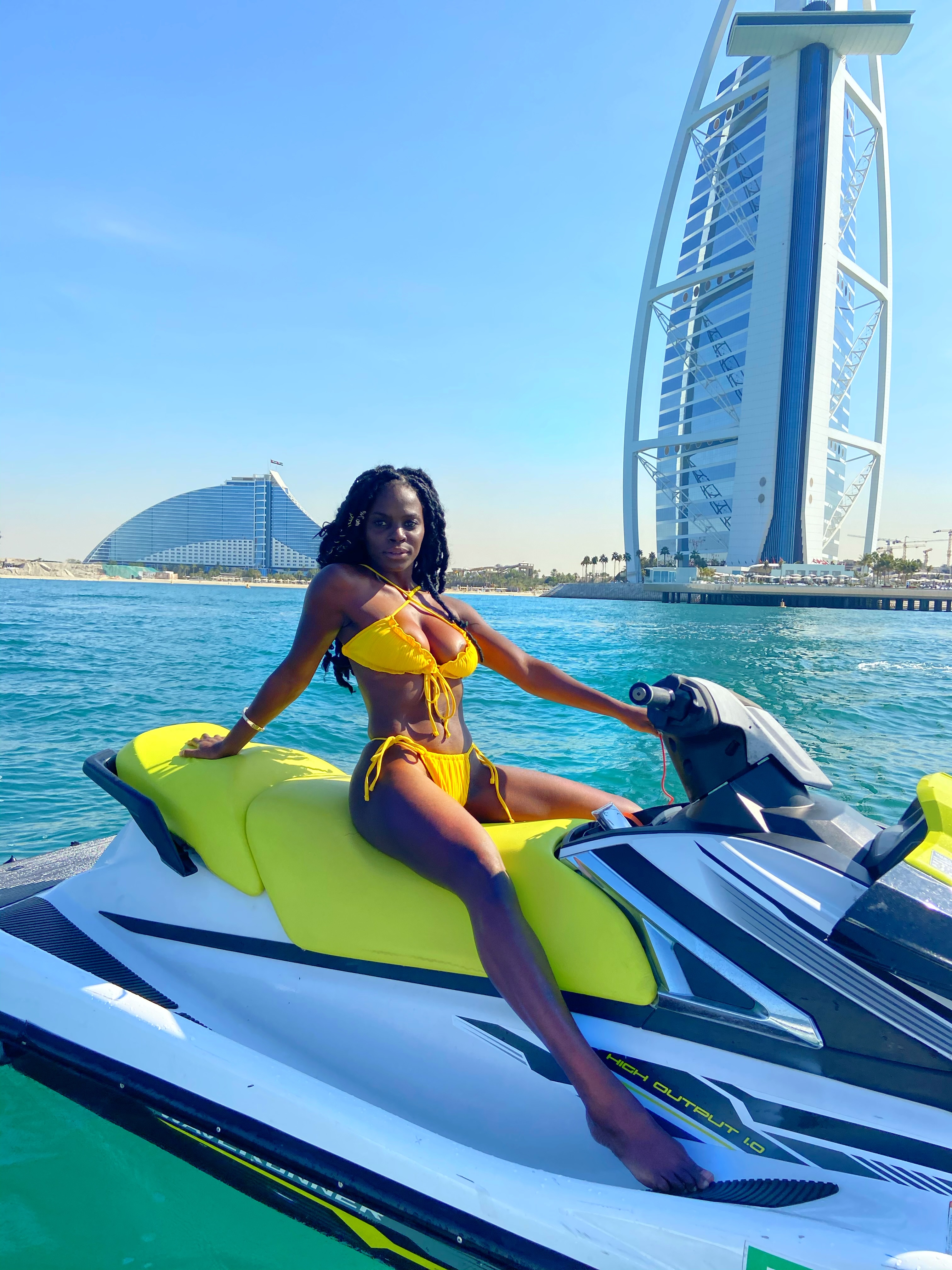 Neola Husbands in Dubai, UAE — Black woman on a jet ski in yellow bikini, Burj Al Arab behind, pandemic-era travel