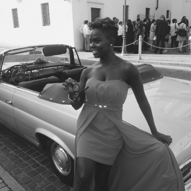Neola Husbands in Brescia, Italy — Black woman in coral dress beside a vintage Mercedes wedding car, Italian wedding turned Mafia run-in