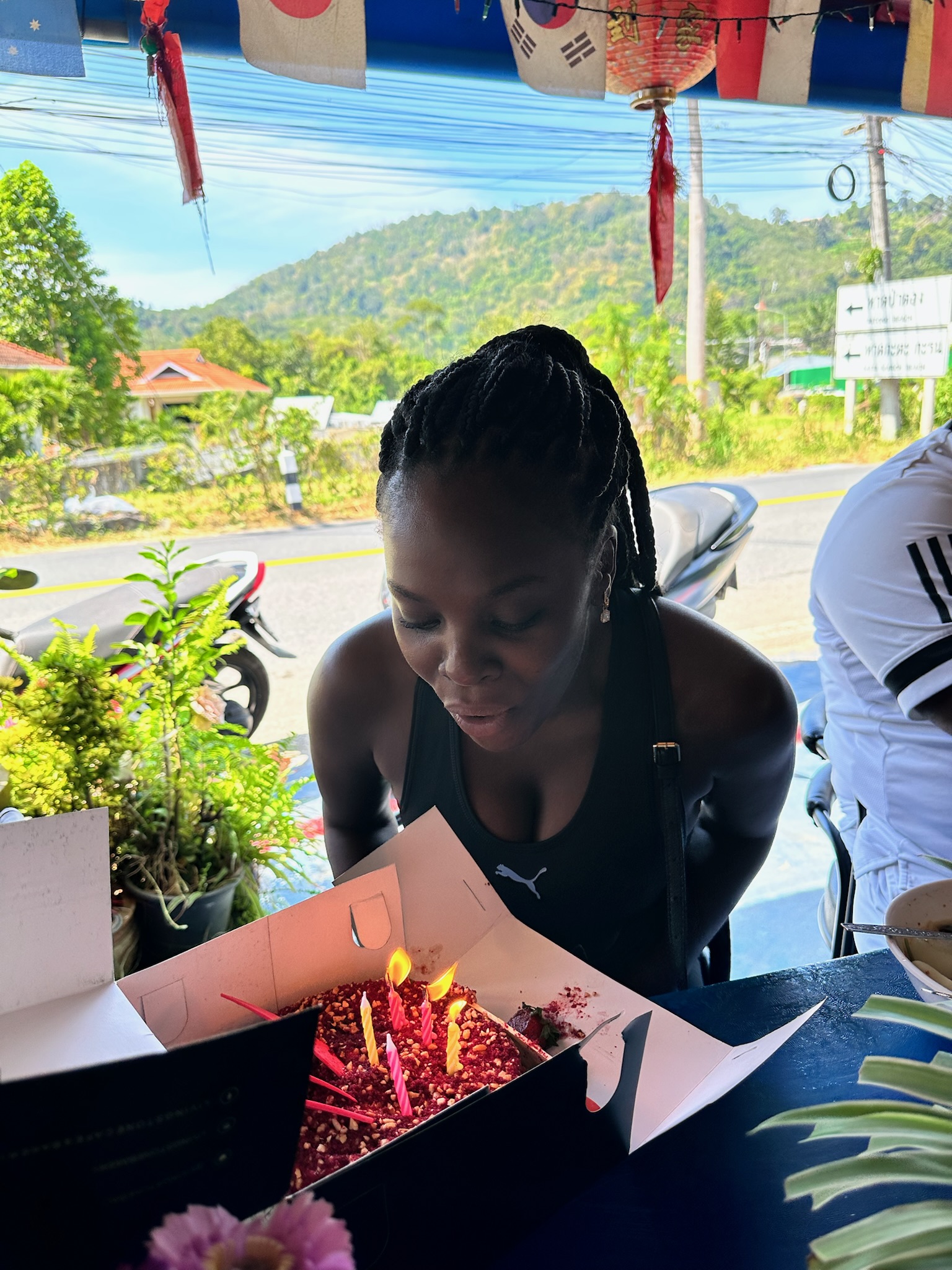 Neola Husbands in Rawai, Thailand — blowing out birthday candles roadside, the cake travelled from Bali to Phuket